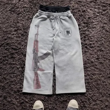 Light grey sweatpants laid flat on a dark carpet, with a small print on one thigh.