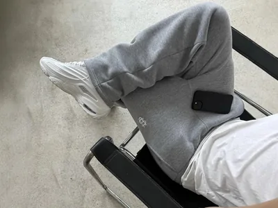 Grey joggers worn with white trainers, seated on a metal chair
